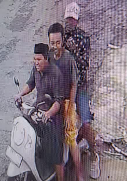 Keterangan Gambar: kedua pria (pelaku) itu dengan ciri-ciri pengendara memakai peci, baju hitam lengan panjang, bawahan sarung dan teman pelaku baju hitam lengan panjang motif bulatan putih, celana pendek jeans bertopi putih, Korban di tengah