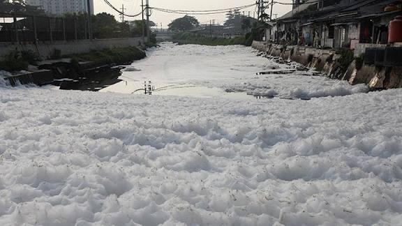 Fenomena busa putih menutupi permukaan Sungai Kalisari Damen, Surabaya akibat limbah deterjen rumah tangga.