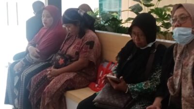 Sejumlah perempuan paruh baya duduk berjejer di bangku ruang tunggu kantor PLN dengan latar belakang logo PLN