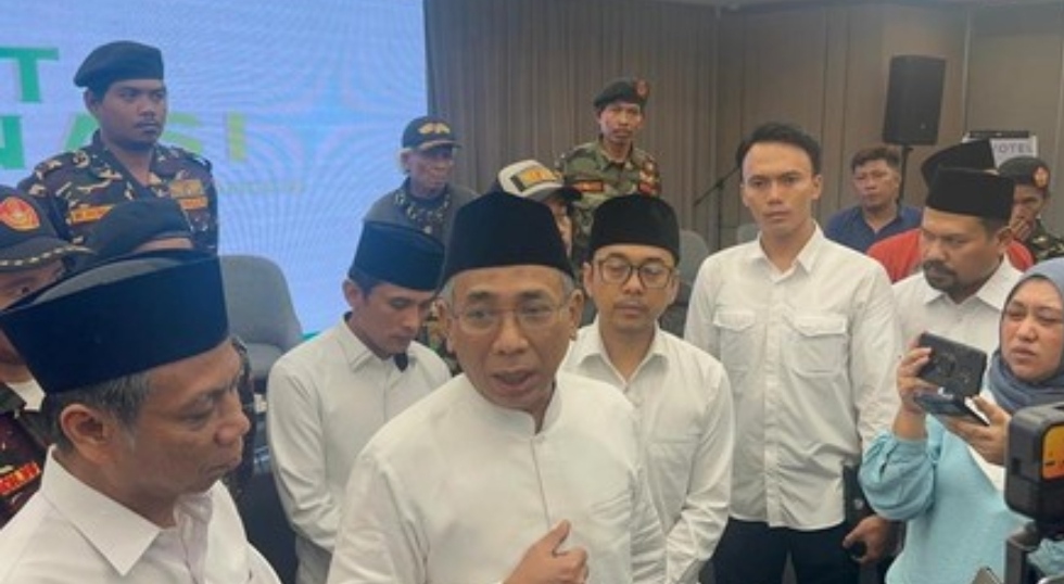 "Ketua Umum PBNU, KH Yahya Cholil Staquf (tengah, berbaju putih dan berpeci), sedang memberikan keterangan kepada wartawan, didampingi oleh Sekjen PBNU Saifullah Yusuf (kiri) dan dikelilingi pengurus NU lainnya serta anggota Banser berseragam."