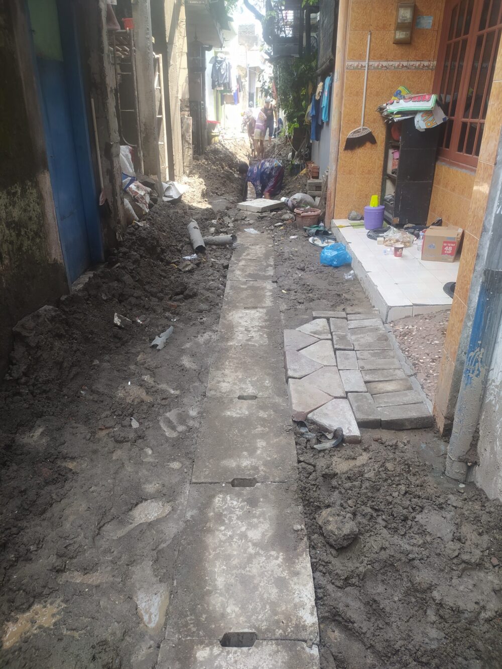 Kondisi proyek pembangunan jalan paving dan saluran air di Rungkut Kidul II Gang Makam Surabaya yang masih berupa tanah berlumpur dan belum selesai dikerjakan melewati batas kontrak.