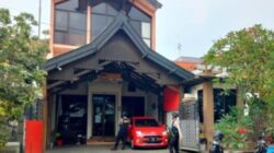 Dua petugas kepolisian bersenjata lengkap berjaga di depan pintu masuk sebuah gedung kantor berlantai dua saat berlangsungnya proses penggeledahan.