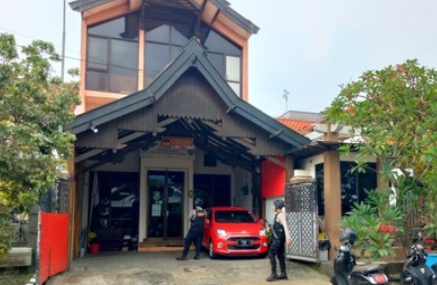 Dua petugas kepolisian bersenjata lengkap berjaga di depan pintu masuk sebuah gedung kantor berlantai dua saat berlangsungnya proses penggeledahan.