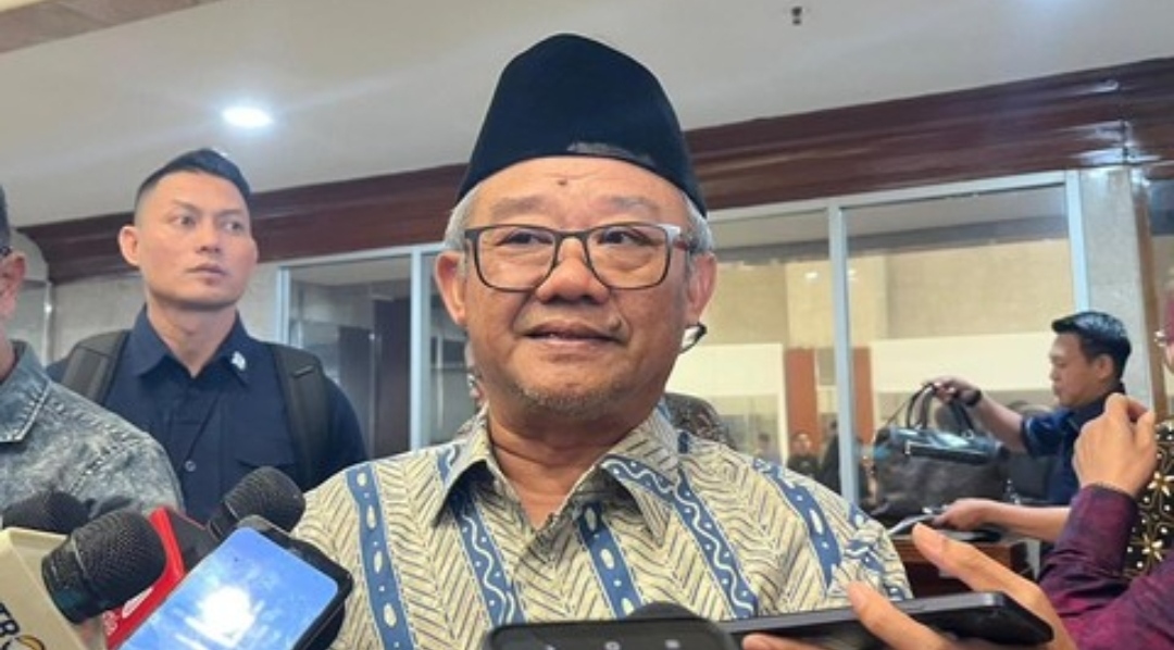 Mendikdasmen Abdul Mu'ti mengenakan kemeja batik dan peci hitam, sedang berbicara di podium dengan latar belakang spanduk Musyawarah Nasional XX IKAPI Tahun 2025.