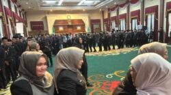Gubernur Khofifah Indar Parawansa (berkerudung abu-abu di tengah depan) berjalan menyalami barisan ratusan pejabat Eselon III dan IV yang baru dilantik. Para pejabat mengenakan seragam hitam berbaris rapi di dalam aula besar Gedung Negara Grahadi yang dihiasi tirai merah putih.