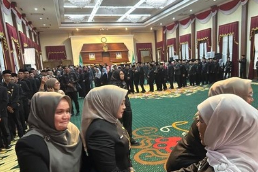 Gubernur Khofifah Indar Parawansa (berkerudung abu-abu di tengah depan) berjalan menyalami barisan ratusan pejabat Eselon III dan IV yang baru dilantik. Para pejabat mengenakan seragam hitam berbaris rapi di dalam aula besar Gedung Negara Grahadi yang dihiasi tirai merah putih.