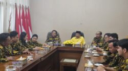 Pria berkemeja kuning memimpin rapat di meja bundar bersama sejumlah orang berseragam loreng AMPG di dalam ruangan.