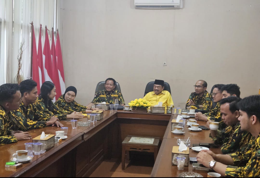 Pria berkemeja kuning memimpin rapat di meja bundar bersama sejumlah orang berseragam loreng AMPG di dalam ruangan.