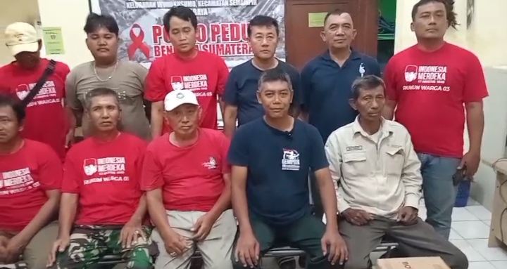 Sekelompok pria berfoto bersama di depan spanduk bertuliskan "Posko Peduli Bencana Sumatera" di dalam ruangan. Sebagian besar dari mereka mengenakan kaos merah seragam bertuliskan "Rukun Warga 03" sebagai identitas kelompok penggerak kegiatan sosial.