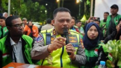 Kakorlantas Polri Irjen Pol Agus Suryonugroho berbicara menggunakan mikrofon saat duduk bersama sejumlah pengemudi ojek online yang mengenakan jaket hijau di sebuah warung kopi.