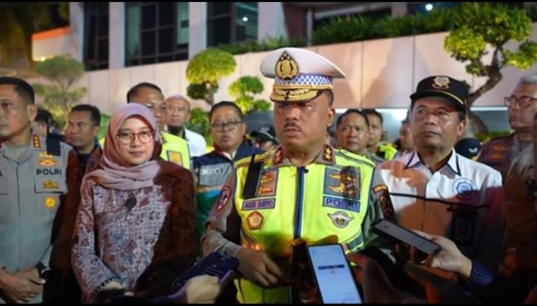 Kakorlantas Polri Irjen Pol Agus Suryonugroho memberikan keterangan pers kepada awak media didampingi pejabat wanita dan jajaran kepolisian lainnya. Ia mengenakan seragam dinas lengkap dengan topi putih saat diwawancara di lokasi terbuka pada malam hari.