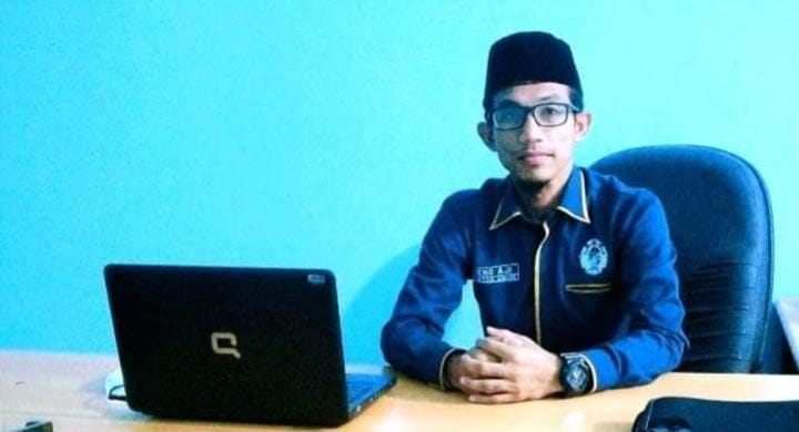 Ketua Umum DPP KAMPUD Seno Aji duduk di belakang meja kerja dengan laptop terbuka, mengenakan kemeja organisasi berwarna gelap dan peci, berlatar dinding biru.