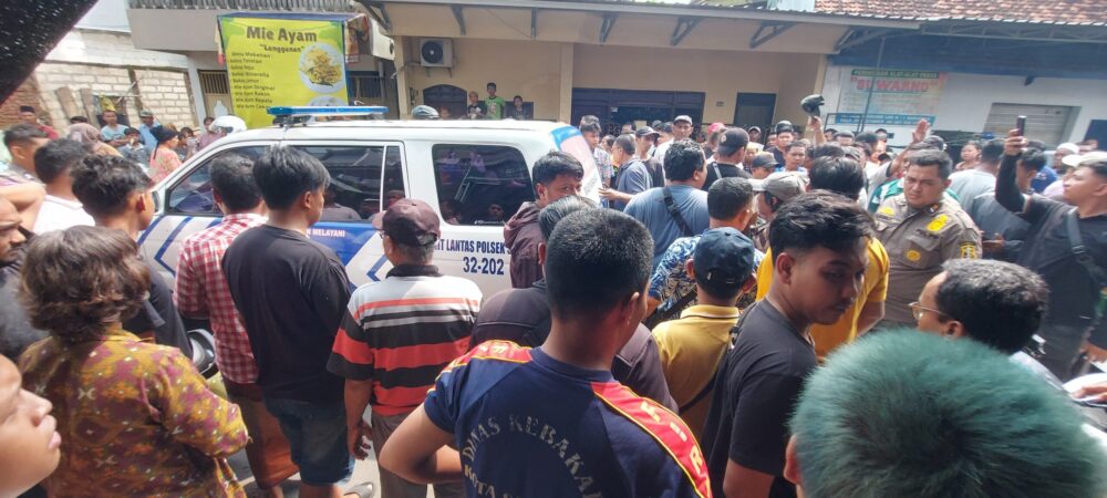 Kerumunan warga mengelilingi sebuah mobil patroli kepolisian di kawasan permukiman, dengan petugas terlihat berada di tengah keramaian.