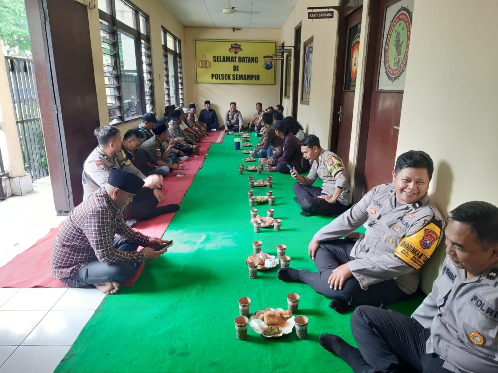 Sejumlah anggota kepolisian dan warga duduk berhadapan di lorong Mapolsek Semampir dengan alas karpet hijau dan merah, tampak hidangan sederhana tersaji di tengah sebagai bagian dari suasana kebersamaan.