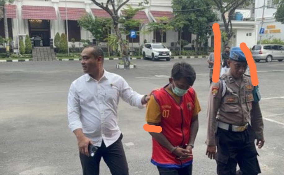 Tersangka penganiayaan berinisial AK mengenakan rompi tahanan merah dan masker hijau digiring petugas kepolisian di halaman Mapolrestabes Surabaya