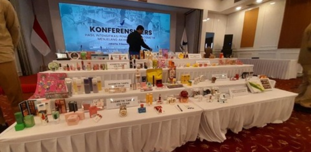 Deretan meja panjang menampilkan berbagai merek kosmetik ilegal hasil sitaan yang ditata bertingkat dalam acara konferensi pers BPOM, dengan layar latar belakang bertuliskan "Konferensi Pers Hasil Intensifikasi Pengawasan Kosmetik Menjelang Akhir Tahun 2025".