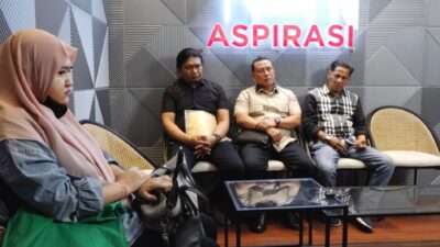 Empat orang duduk di kursi rotan dalam ruang mediasi dengan latar belakang dinding abu-abu berlogo lampu neon merah bertuliskan "ASPIRASI".