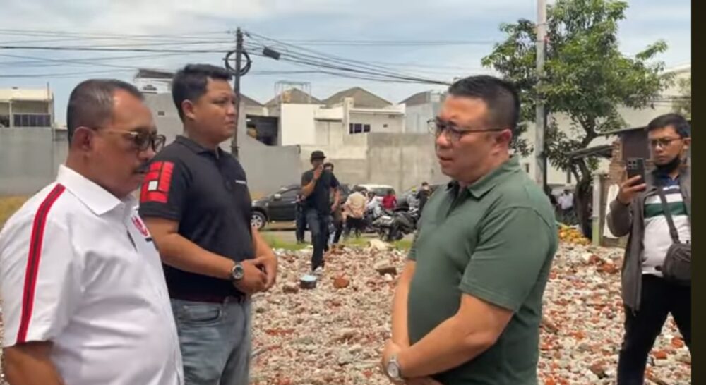 Seorang pria berbaju hijau berdiri berhadapan dengan Wakil Wali Kota Surabaya di area puing-puing bangunan yang telah dirobohkan, disaksikan beberapa orang di sekitarnya.