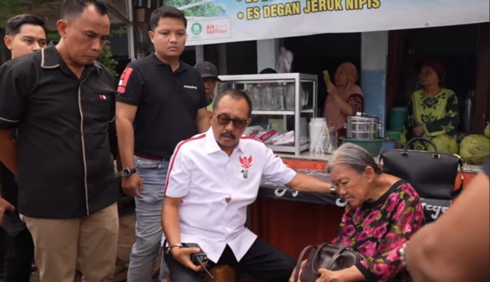 Wakil Wali Kota Surabaya Armuji duduk di samping seorang lansia perempuan sambil memegang bahunya, dikelilingi beberapa pria, di depan lapak sederhana kawasan permukiman.