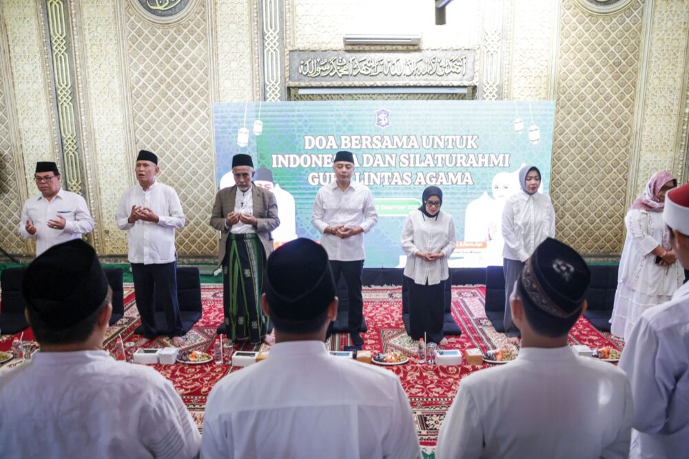 Wali Kota Surabaya Eri Cahyadi beserta istri dan para tokoh agama berdiri memanjatkan doa di depan panggung acara bertuliskan "Doa Bersama untuk Indonesia". Mereka tampak khusyuk berdoa di dalam ruangan berkarpet merah dengan latar dinding bernuansa emas.