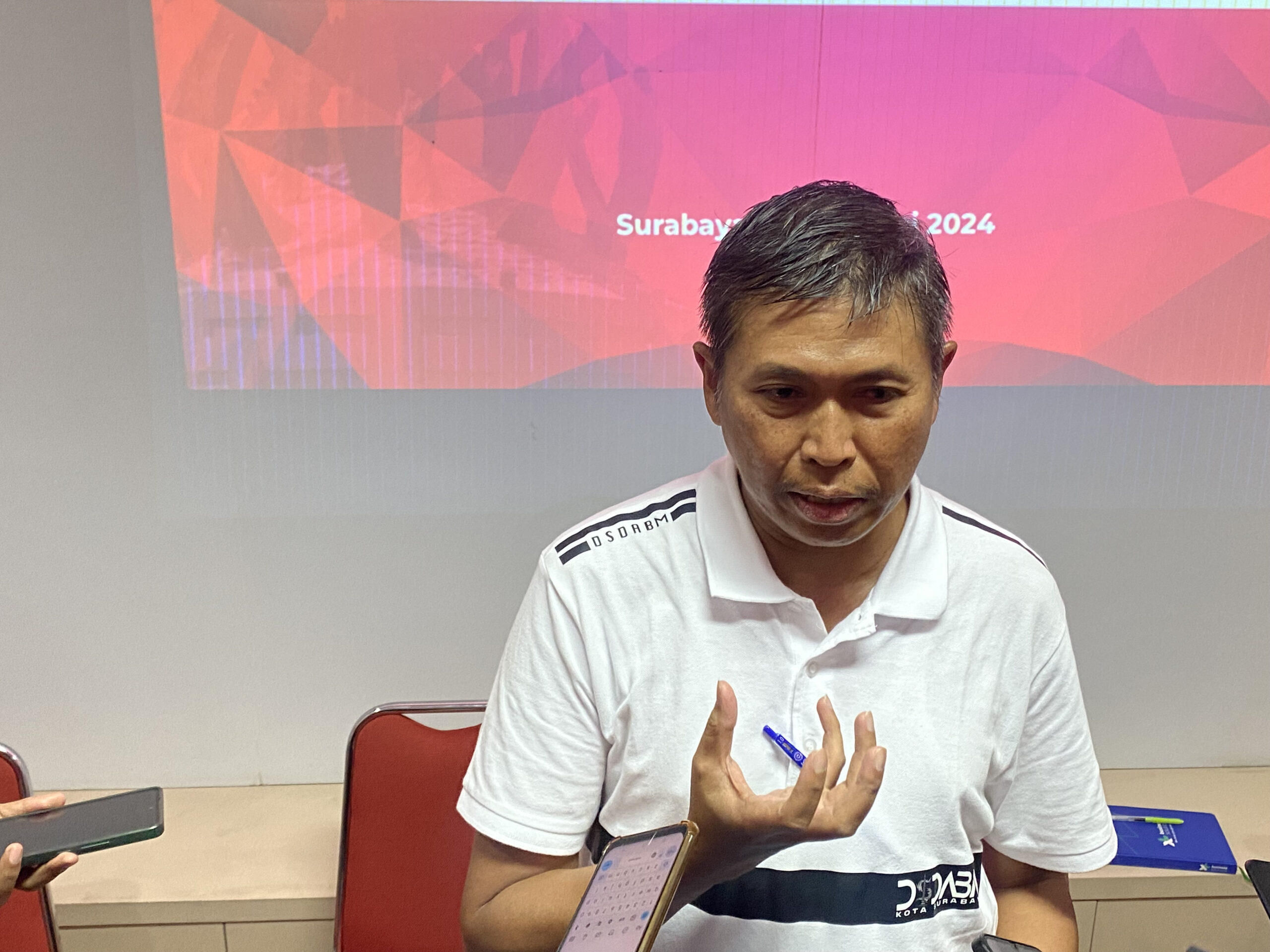 Kepala DSDABM Surabaya Syamsul Hariadi mengenakan kemeja putih berlogo dinas sedang memberikan keterangan pers kepada wartawan mengenai penanganan banjir.