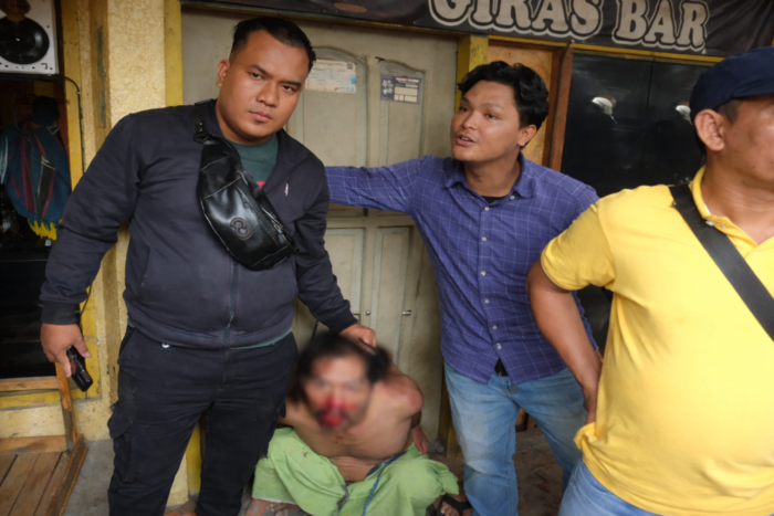 Seorang pria terduga pelaku pencurian sepeda motor tampak duduk di lantai dengan kondisi terluka, dikelilingi beberapa warga di depan bangunan kawasan permukiman.