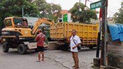 Satu unit ekskavator kuning merek Hyundai dan truk pengangkut material disiagakan di persimpangan jalan Tegal IV yang bertanda "Batas Santri", diawasi oleh petugas lapangan.