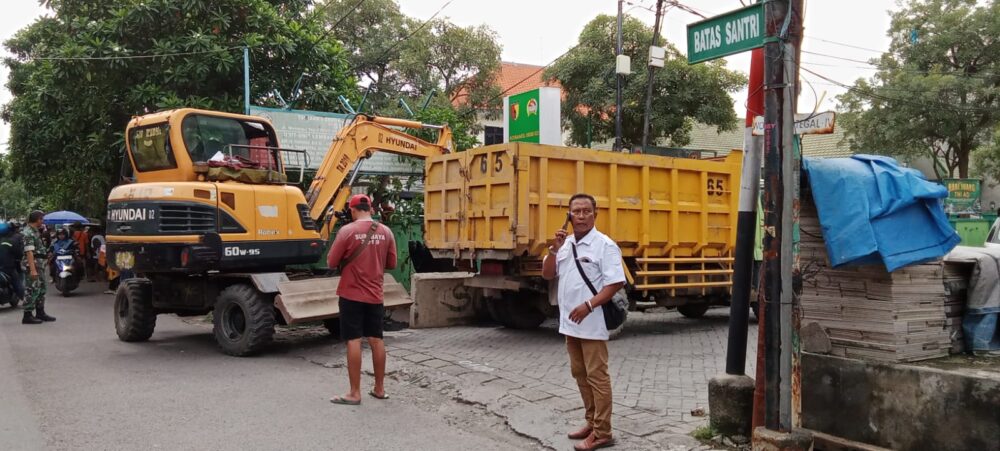 Satu unit ekskavator kuning merek Hyundai dan truk pengangkut material disiagakan di persimpangan jalan Tegal IV yang bertanda "Batas Santri", diawasi oleh petugas lapangan.