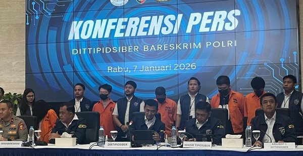 Suasana konferensi pers Dittipidsiber Bareskrim Polri dengan latar layar biru bertuliskan tanggal 7 Januari 2026. Sejumlah pejabat kepolisian duduk di meja depan, sementara beberapa tersangka berbaju oranye berdiri di belakang dengan dijaga petugas.