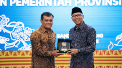 Gubernur Lampung dan Gubernur Jawa Tengah berdiri berdampingan sambil memegang plakat cenderamata bersama-sama dan tersenyum ke arah kamera di depan latar panggung acara.