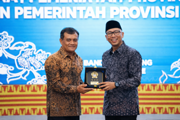 Gubernur Lampung dan Gubernur Jawa Tengah berdiri berdampingan sambil memegang plakat cenderamata bersama-sama dan tersenyum ke arah kamera di depan latar panggung acara.