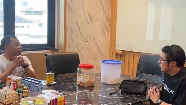 Dua pria duduk berhadapan di sebuah meja marmer; pria di sebelah kiri mengenakan kaus putih sementara pria di sebelah kanan mengenakan kaus hitam bertuliskan Givenchy dan bando.