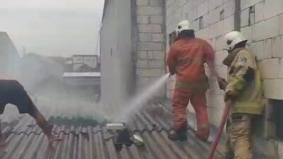 Petugas Dinas Pemadam Kebakaran dan Penyelamatan Kota Surabaya terlihat sedang melakukan upaya pemadaman dan pembasahan di atas atap rumah warga yang terbakar di Jalan Dukuh Bulak Banteng Timur pada Selasa siang