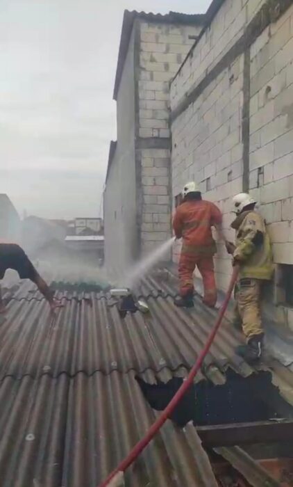 Petugas Dinas Pemadam Kebakaran dan Penyelamatan Kota Surabaya terlihat sedang melakukan upaya pemadaman dan pembasahan di atas atap rumah warga yang terbakar di Jalan Dukuh Bulak Banteng Timur pada Selasa siang